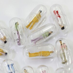 Op de afbeelding: Een verzameling doorzichtige capsules met miniatuurfiguren erin. De figuren zijn gekleed in verschillende kleuren en stijlen, waaronder geel, rood, groen en roze.