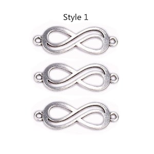 Op de afbeelding: Drie zilverkleurige oneindigheidssymboolbedels met kleine lussen aan elk uiteinde. De bedels worden weergegeven tegen een witte achtergrond. De tekst "Style 1" staat bovenaan de afbeelding.