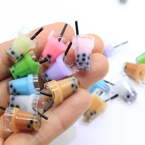 May include: Assortment of colorful miniature plastic bubble tea cups with black straws. The cups are filled with a variety of colors and have black boba pearls.