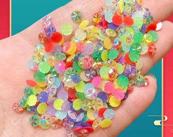 May include: A handful of colorful, iridescent rhinestones in various shapes and sizes. The rhinestones are primarily round and faceted, with a mix of colors including red, yellow, green, and purple. These decorative embellishments are ideal for crafts and DIY projects.