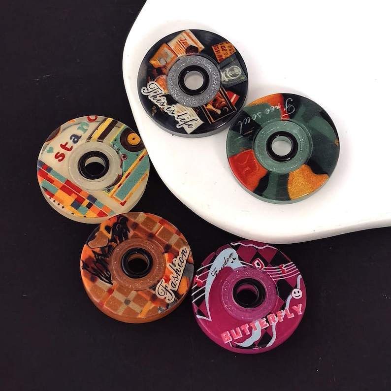 May include: Five colorful, circular decorative objects with central holes. Designs include the words "This is life", "Free soul", "Fashion", and "Butterfly". The objects have various patterns and colors, including orange, pink, and blue.