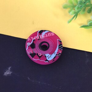 May include: A pink roller skate wheel with the word "BUTTERFLY" printed around the edge. The wheel has a black and white design with the word "Freedom" in a cursive font. The wheel has a black center.
