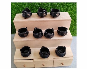 Op de afbeelding: Tien miniatuur zwarte keteltjes met handvatten, gerangschikt op een driedelig houten rek.