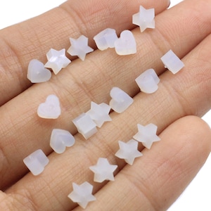 May include: A collection of white resin beads in various shapes, including stars, hearts, and squares. The beads are small and have a smooth, polished finish.