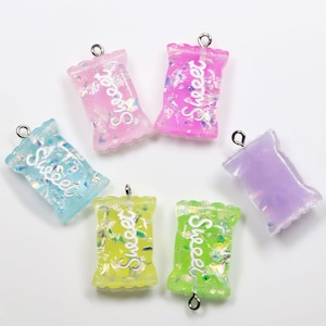 May include: Six colorful candy bag charms with a silver loop for hanging. Each charm has a glittery finish and the word "Sweet" written on it.