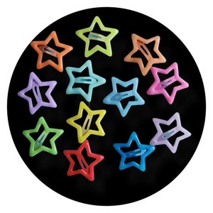 Puede incluir: Una colección de horquillas para el pelo con forma de estrella en varios colores, como naranja, verde, rosa, azul, amarillo y morado. Las horquillas están dispuestas sobre un fondo negro. Cada horquilla tiene un cierre metálico.