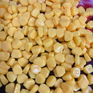 May include: A close-up image of a pile of bright yellow corn kernels. The kernels are glossy and appear fresh, with a slightly irregular shape. The image is well-lit, highlighting the texture and colour of the corn.