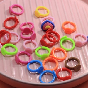 May include: A collection of colorful plastic rings with different shapes and designs. The rings are arranged on a pink surface.