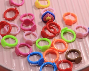 May include: A collection of colorful plastic rings with different shapes and designs. The rings are arranged on a pink surface.
