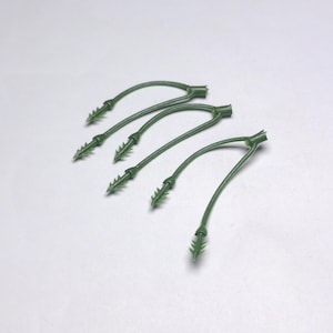 May include: Four green plastic plant ties with a curved design and pointed barbs. These ties are designed to secure plants to stakes or supports. The ties are made of a durable, flexible plastic.