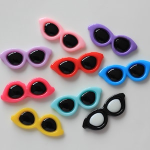 Puede incluir: Surtido de gafas de sol de plástico de colores con lentes negros. Las gafas de sol son de varios colores, incluyendo rosa, morado, rojo, azul, turquesa, amarillo y negro.