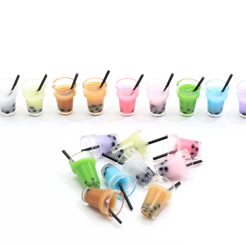 May include: A set of 12 miniature plastic cups with black straws filled with colourful bubble tea. The cups are arranged in a row and scattered on a white surface.