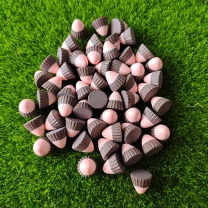 Könnte beinhalten: Eine Ansammlung kleiner, kegelförmiger Objekte mit zweifarbigem Design, bestehend aus einer glatten, hellrosa Spitze und einer dunkelgrauen, gerippten Basis. Jedes Teil hat eine flache, kreisförmige Oberseite und eine geriffelte Oberfläche.