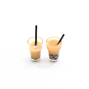 May include: Two clear plastic cups with black straws filled with a light brown liquid and black boba pearls.