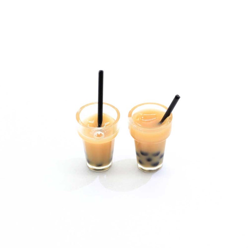 May include: Two clear plastic cups with black straws filled with a light brown liquid and black boba pearls.