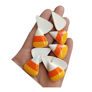 以下が含まれることがあります： 白、オレンジ、黄色のセラミック製キャンディーコーンチャーム8個セット。チャームはキャンディーコーンの形をしており、光沢のある仕上げになっています。