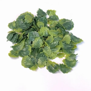 Puede incluir: Un montón de pequeñas hojas de plástico en tonos verdes y verde amarillento. Las hojas tienen un patrón de vetas detallado y están dispersas sobre una superficie blanca. Estas hojas decorativas son adecuadas para proyectos de manualidades.