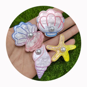 May include: Four colorful resin seashell and starfish charms with pearl accents. The charms are white with pink, purple, blue, and yellow accents.