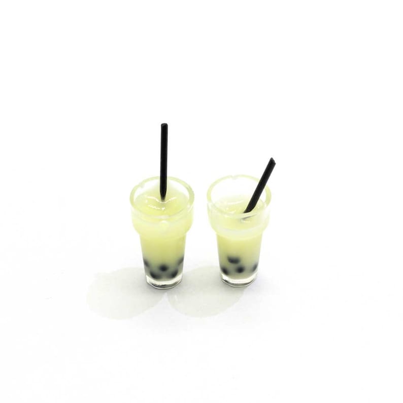 May include: Two clear plastic cups with black straws filled with a light yellow liquid and black boba pearls.