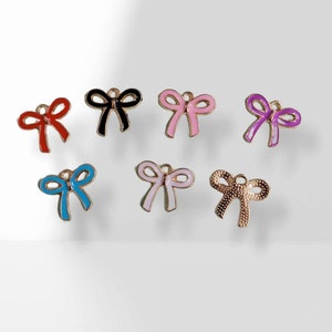 Peut inclure: Assortiment de sept breloques en forme de nœud de couleurs différentes avec des accents en métal doré. Les nœuds sont en rouge, noir, rose, violet, bleu clair, rose clair et or.