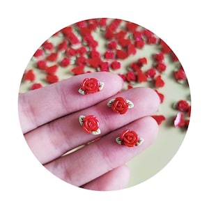 Peut inclure: Quatre embellissements de fleurs de rose rouges avec des feuilles vertes. Les roses sont sur une main, et il y a beaucoup d'autres roses éparpillées sur une surface jaune clair.