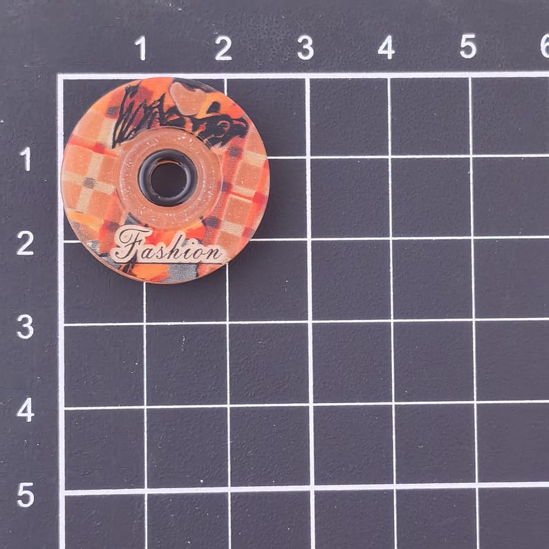 May include: A round, orange and brown decorative wheel with a central black hole. The wheel has a plaid pattern and a graphic design. The word "Fashion" is printed on the wheel.