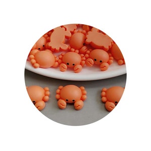 May include: A group of small, orange, plastic crab figurines. The crabs have black eyes and are arranged on a white plate.
