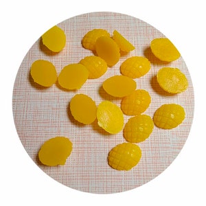 May include: A collection of yellow gummy sweets shaped like pineapples. The sweets are arranged on a pink and white patterned surface.