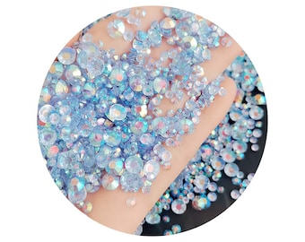 May include: A close-up of a hand holding a large quantity of iridescent blue rhinestones. The rhinestones are scattered on a black surface.