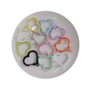 May include: Assortment of colorful heart-shaped metal clasps. The clasps are in various colors, including yellow, pink, orange, light blue, and black.