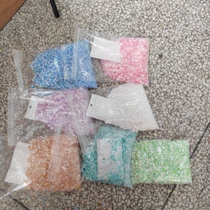 May include: Seven bags of iridescent sequins in various colors, including pink, blue, green, white, and purple. The sequins are packaged in clear plastic bags with white labels.