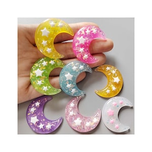 May include: Assortment of colorful crescent moon shaped resin charms with white star accents. The charms have a glittery finish.