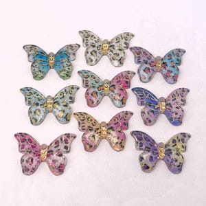 May include: Nine decorative butterfly embellishments in various colors, including blue, purple, pink, and gold. Each butterfly features a gold-colored center and detailed wing patterns, with a leopard print design.