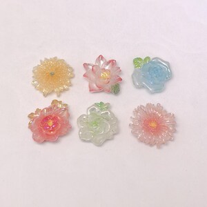 以下が含まれることがあります： さまざまな色の半透明樹脂製の花の装飾が6つ。 花には、黄色のデイジー、ピンクの蓮、青いバラ、ピンクのシャクヤク、緑のバラ、ピンクのデイジーが含まれます。 各花は詳細なデザインです。