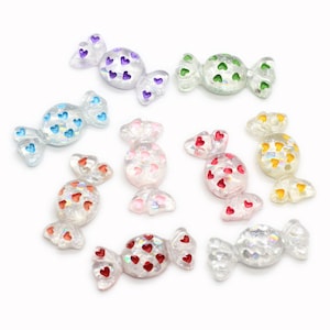 May include: Assortment of ten candy-shaped resin embellishments with a holographic finish. Each candy is decorated with small hearts in various colors, including red, pink, blue, green, purple, and yellow.