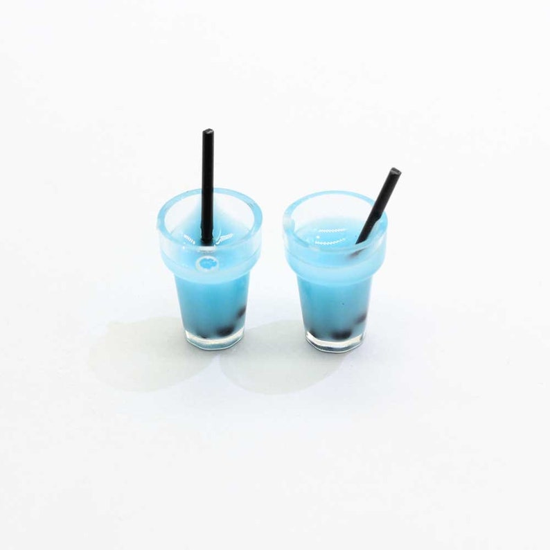 May include: Two miniature plastic cups filled with blue liquid and black boba pearls. Each cup has a black straw sticking out of the top.