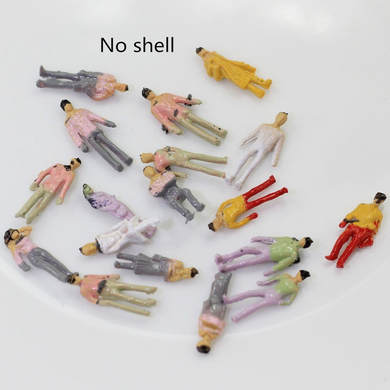 Op de afbeelding: Een verzameling van 15 miniatuur plastic figuren in verschillende kleuren, waaronder roze, geel, rood, groen en wit. De figuren staan ​​allemaal in verschillende poses en zijn gerangschikt op een wit oppervlak. De tekst "No shell" is zichtbaar in de linkerbovenhoek van de afbeelding.