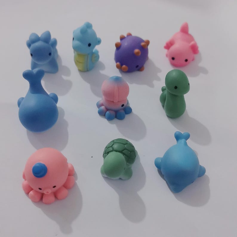 May include: A set of ten small, colourful, animal-shaped figurines. The figurines are made of a soft, rubbery material and are perfect for playing or decorating. The set includes a blue whale, a pink octopus, a green turtle, a blue dinosaur, a purple spiky creature, a pink axolotl, a green snake, a blue and pink octopus, and a yellow and orange seahorse.