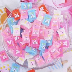 May include: A collection of small, colorful, glittery, plastic candy bags with bunny faces and the word "CHIPS" printed on them.
