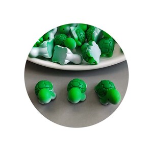 May include: A group of small green turtle figurines, some with their shells facing up and some with their shells facing down. Three of the turtles are shown in the foreground, facing the camera.