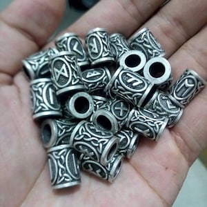 May include: A collection of silver-toned metal beads with intricate designs and runes. Each bead features a different rune symbol.