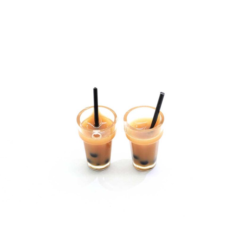May include: Two clear plastic cups filled with brown bubble tea with black tapioca pearls. Each cup has a black straw sticking out of the top.