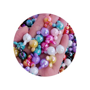 K&ouml;nnte beinhalten: Eine Sammlung von regenbogenfarbenen, pastellfarbenen Plastikperlen mit einem Hasendesign. Die Perlen sind in verschiedenen Farben, darunter rosa, blau, lila, gr&uuml;n und gelb.