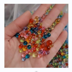 May include: A hand holding a variety of colorful water beads. The beads are translucent and have a slight shimmer to them. They are a popular sensory toy for children.