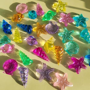 May include: A collection of colorful glass seashells and starfish. The seashells are in various shapes and sizes, and the starfish are all different colors.