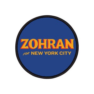 Può includere: Toppa rotonda con sfondo blu e la scritta "ZOHRAN" in arancione, con ombra rossa, e la scritta "FOR NEW YORK CITY" in blu. La toppa ha un bordo nero.