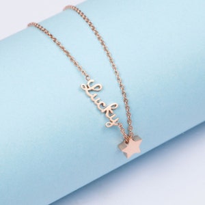 Puede incluir: Un collar de oro rosa con un dije de estrella y la palabra "Lucky".