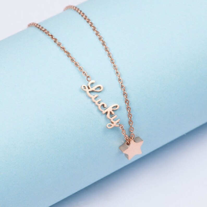 Puede incluir: Un collar de oro rosa con un dije de estrella y la palabra "Lucky".