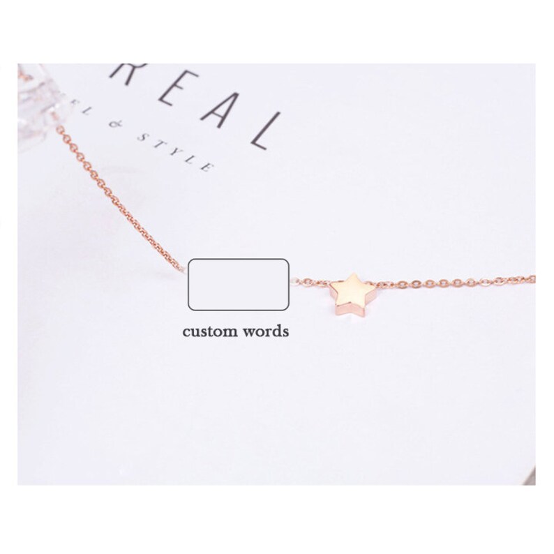 Puede incluir: Un delicado collar de color dorado con un peque&ntilde;o dije en forma de estrella. La cadena es fina y presenta un dise&ntilde;o delicado de eslabones. El collar se muestra sobre una superficie blanca con las palabras "REAL & STYLE" visibles en el fondo.