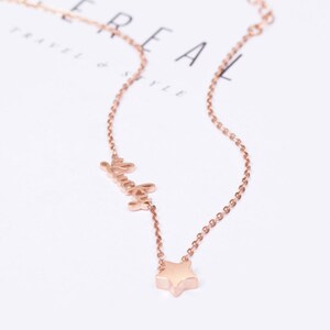 Puede incluir: Un collar de oro rosa con un dije de estrella y la palabra "lucky".